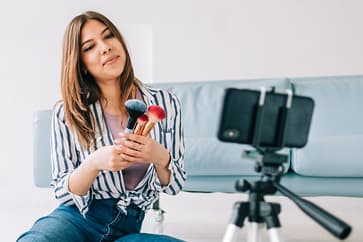 Influenser lager videoinnhold for sosiale medier. Et eksempel på influensermarkedsføring i praksis. Influenser filmer sminkevideo med mobil og stativ som del av influensermarkedsføring på sosiale medier
